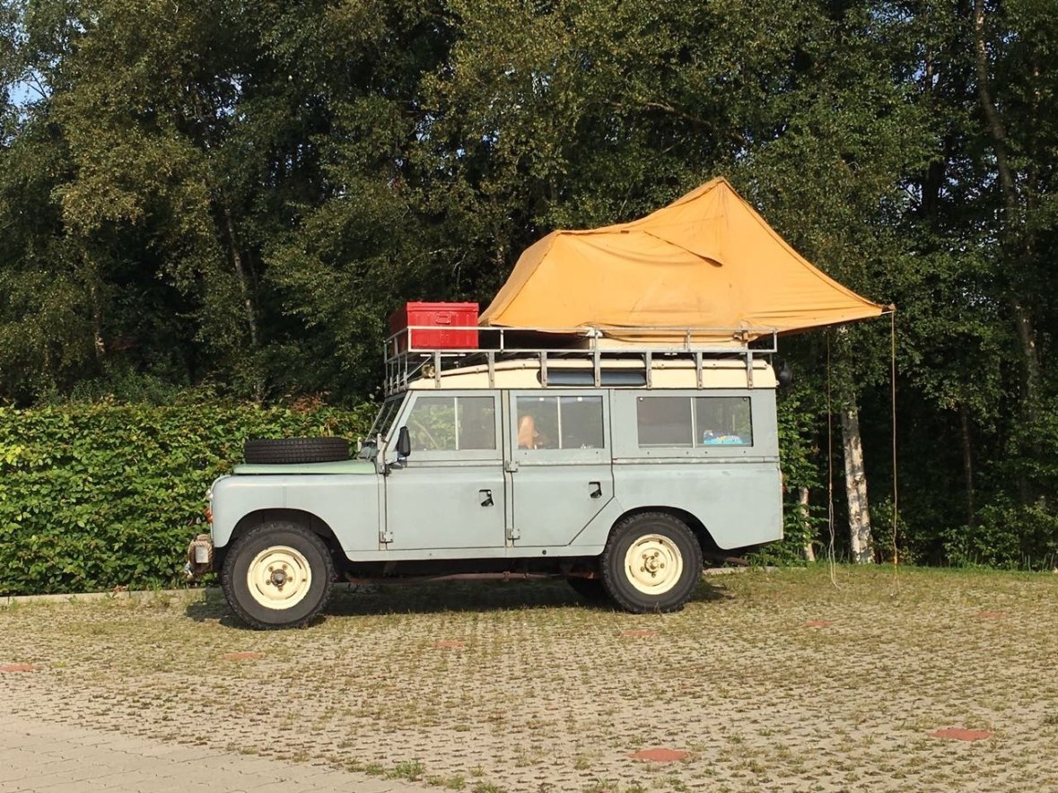 Auf dem Bild sieht man ein "besonderes" Wohnmobil. Es ist ein Blaues großes Auto mit einem gelben Dachzelt oben drauf.