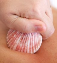 Auf dem Bild sieht man ein Körperteil, der mithilfe einer Muschel und einer Hand massiert wird.